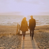 Imagem de um casal de mãos dadas no pôr do sol em um pier de uma praia